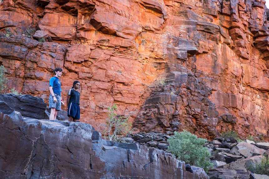 Two young people stand in a rocky red canyon in outback Australia, dwarfed by the landscape around them.
