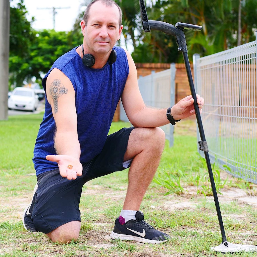 Man kneels beside metal detector holding gold ring.