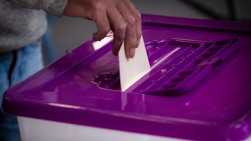 Voter's hand places ballot into ballot box.