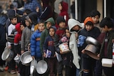 Palestinian children in a queue holding saucepans