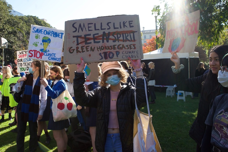 A young protester stands at a climate change rally in Melbourne, holding up a sign.