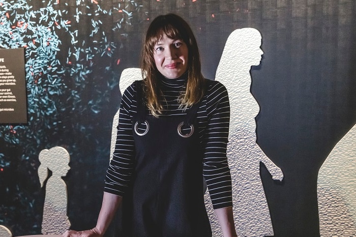 A woman leans her hands on a table with an interactive screen on it within the Gut Exhibition room.