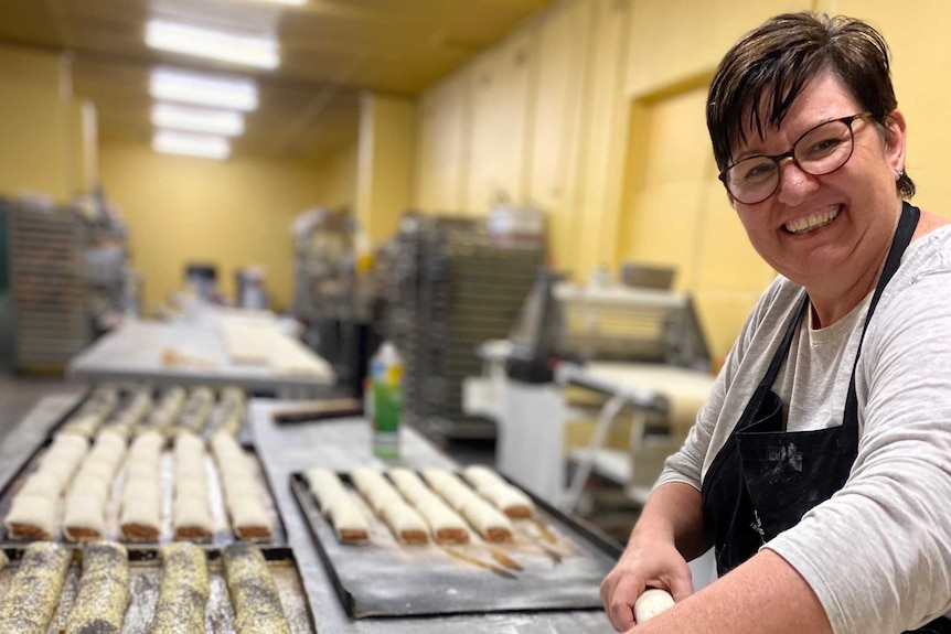 A smiling woman preparing sausage rolls at a bakery