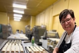 A smiling woman preparing sausage rolls at a bakery.