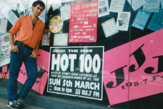 triple j intern Lawrie Zion, who came up with the idea for the countdown, posing by promotional artwork for 2JJJ's Hot 100.