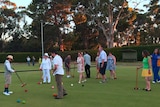 People play croquet in colourful outfits, very relaxed feel on greens with tall trees in background.