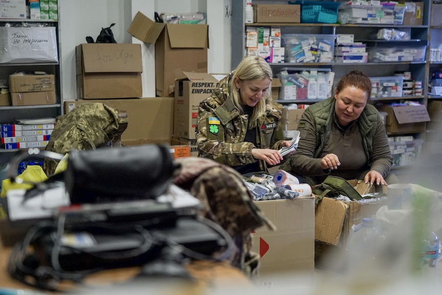 Two women in combat gear packing cardboard boxes
