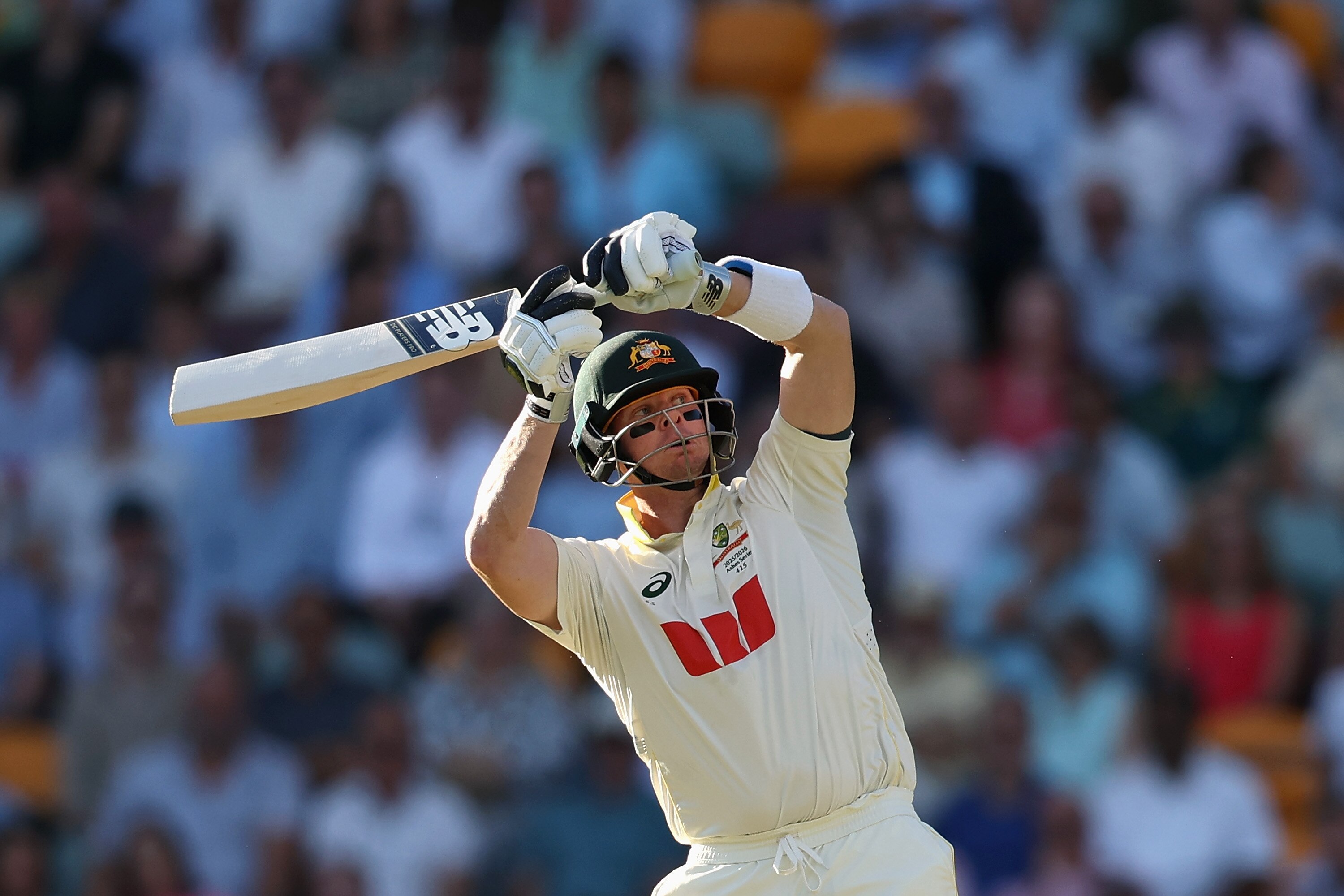 Un jugador de críquet que lleva un casco con líneas negras debajo de los ojos juega un tiro con el bate por encima de su cabeza.