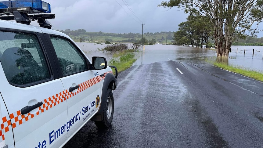 Large white 4 wheel drive with orange checkers pulled to the side of a road, flooded roadway ahead