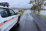 Large white 4 wheel drive with orange checkers pulled to the side of a road, flooded roadway ahead