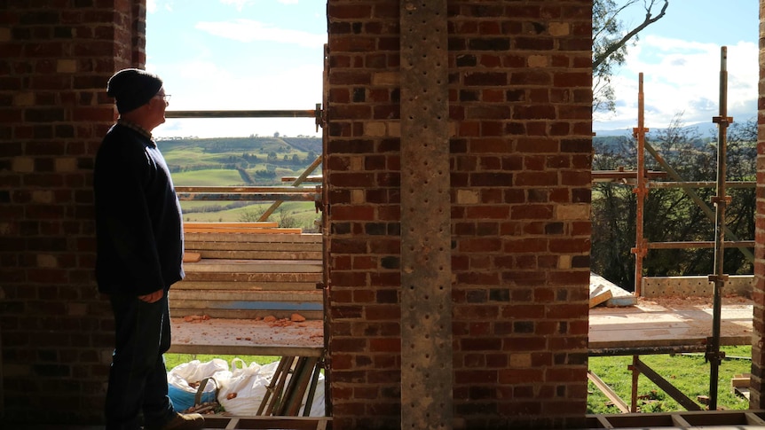 a farmer looks through a brick window out to a field