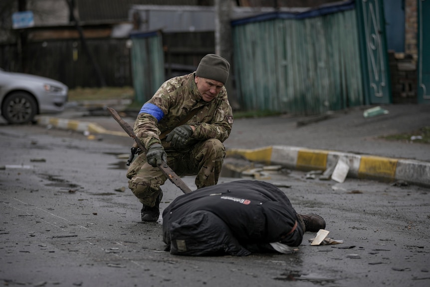 A Ukrainian serviceman pokes the body of a man dressed in civilian clothing with a stick. 