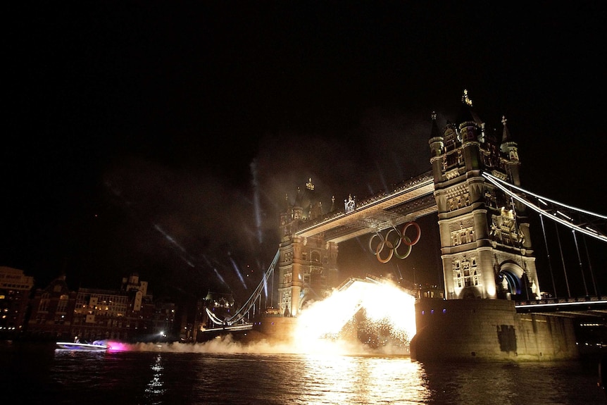 A speedboat carrying the Olympic torch races under Tower Bridge at the Opening Ceremony in London.