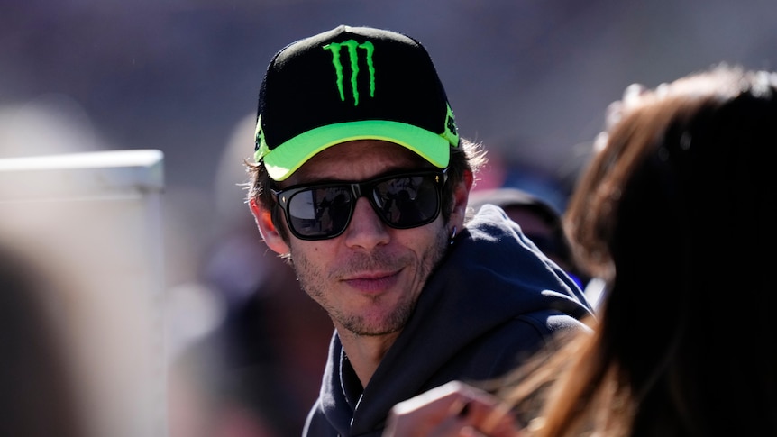 Italian motor sports star Valentino Rossi wears a black and green cap and dark glasses at a race track in Spain.