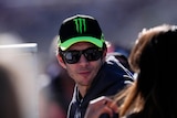 Italian motor sports star Valentino Rossi wears a black and green cap and dark glasses at a race track in Spain.