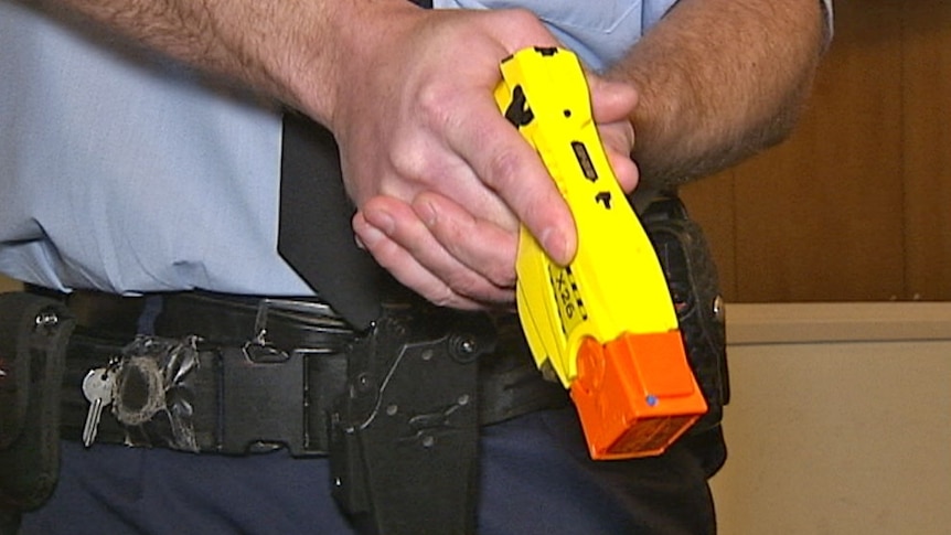 A police officer drawing a Taser from his belt.
