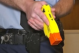 A police officer drawing a Taser from his belt.