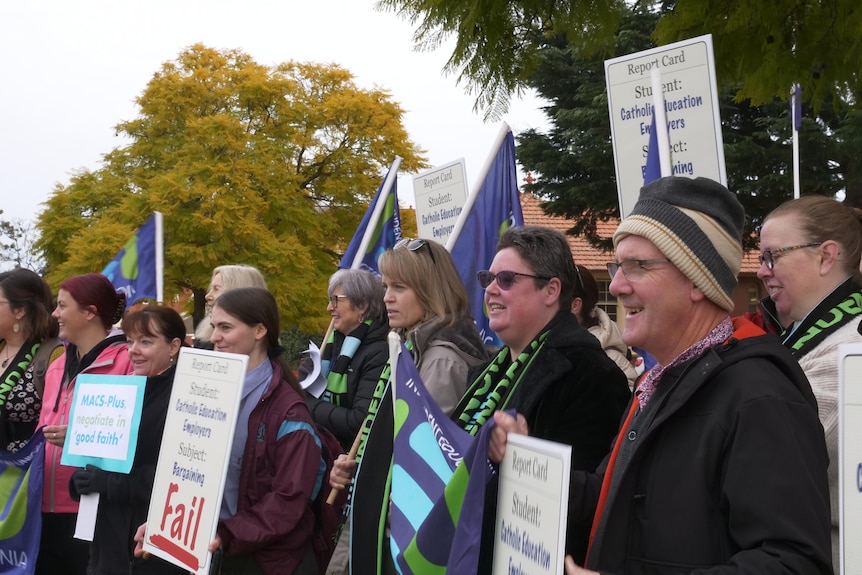 A crowd of teachers holding flags and banners face the school drop off area on a winter morning. 