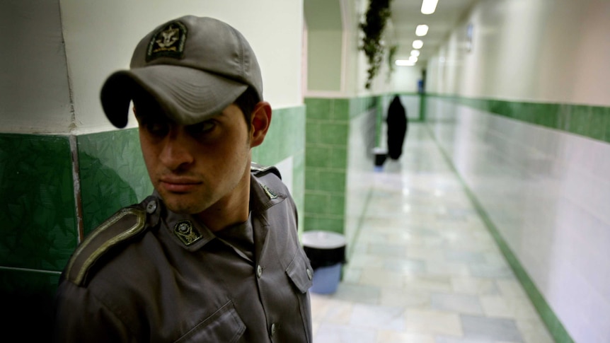 A guard wearing a cap looking from right to left along a corridor inside Evin prison.