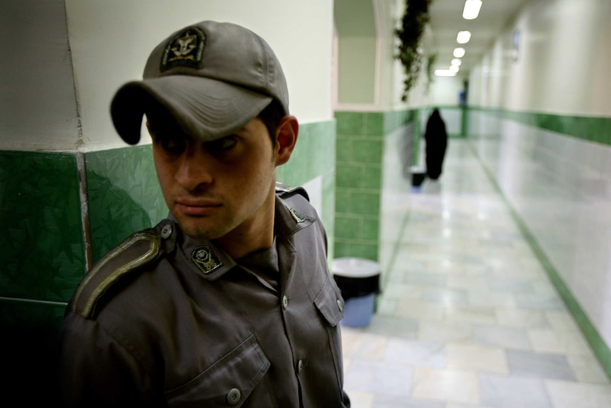 A guard wearing a cap looking from right to left along a corridor inside Evin prison.