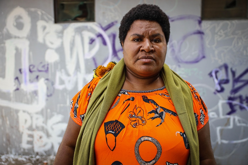 A close up of a PNG woman wearing an orange shirt and green scarf.