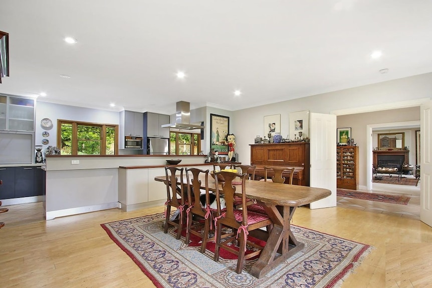 A dining table sits in the middle of an open-plan kitchen and living area with wooden floors.