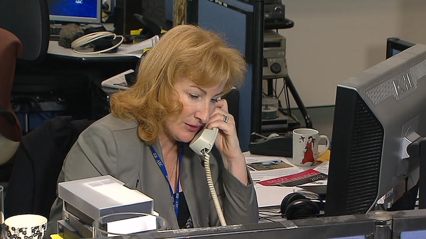 O'Neill on the phone at desk in newsroom.
