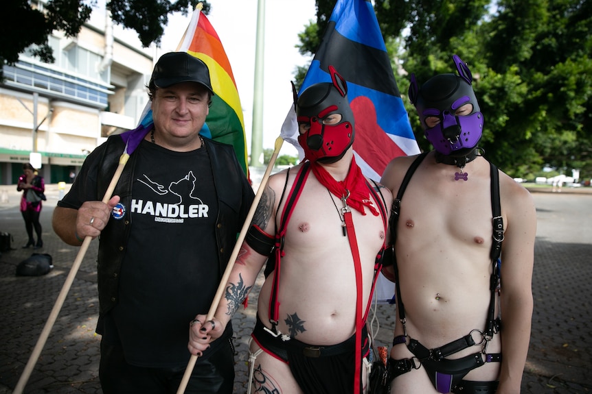 three men two with face masks on and one carrying a rainbow flag