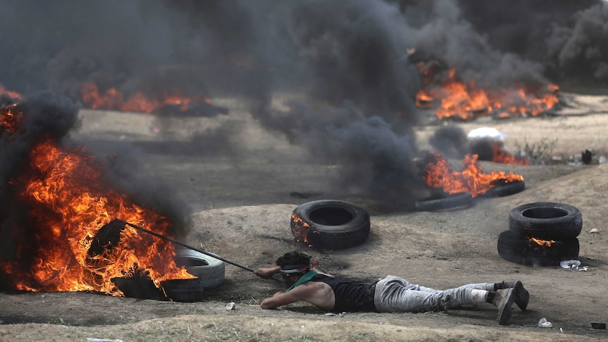 A man lies on the ground as tires burn around him.