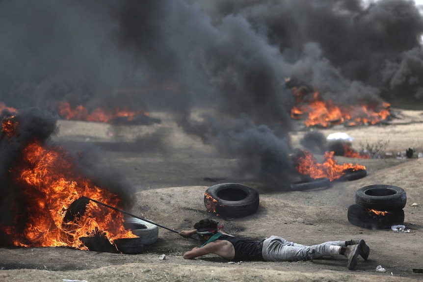 A man lies on the ground as tires burn around him.