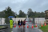 People stand watching flooded waterway