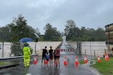 People stand watching flooded waterway