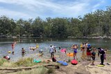 People cool down in the lake in swimmers and board shorts, a blue sky with clouds