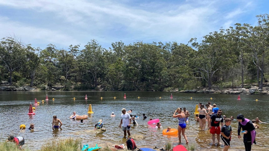 People cool down in the lake in swimmers and board shorts, a blue sky with clouds