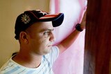 A male asylum seeker wears a baseball cap and looks out a window