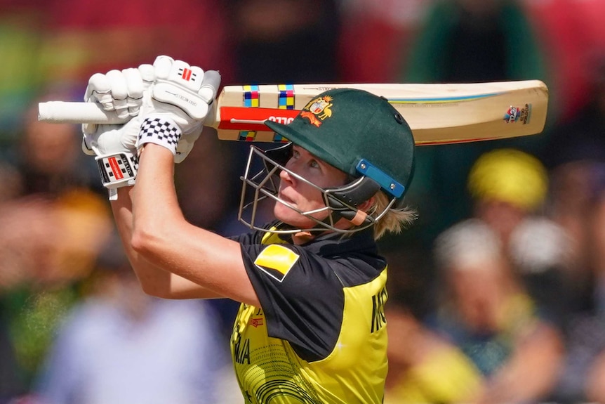 An Australian female cricketer watches a ball after hitting it in the air against New Zealand in Melbourne.