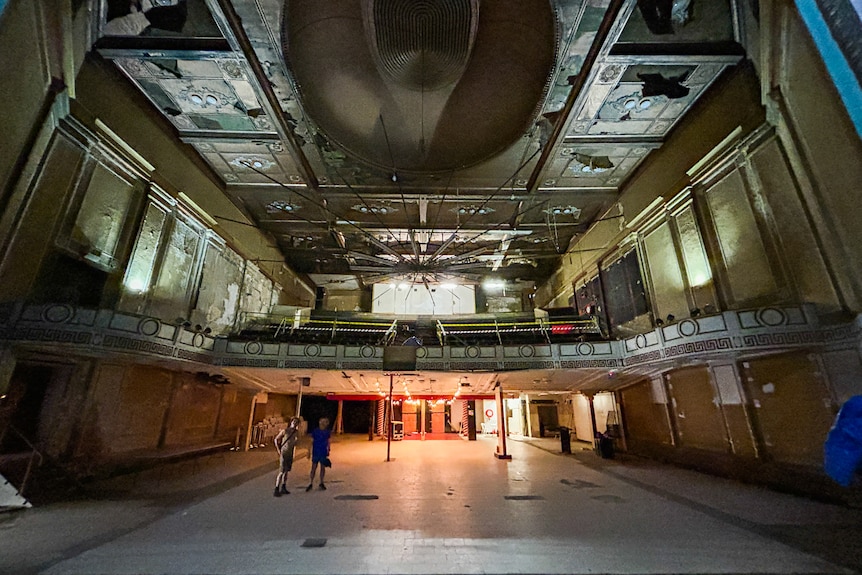 Inside an old theatre with paint peeling and seats removed.