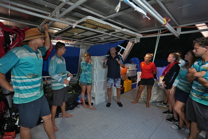 a team of people stand on a boat for a briefing at night time 