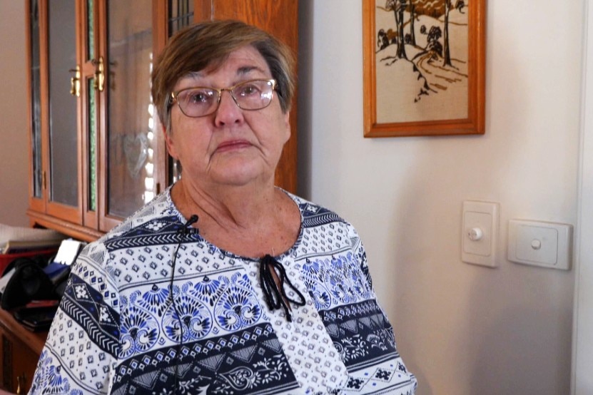 Elderly woman in white and clue blouse, short brown hair and glasses, serious expression