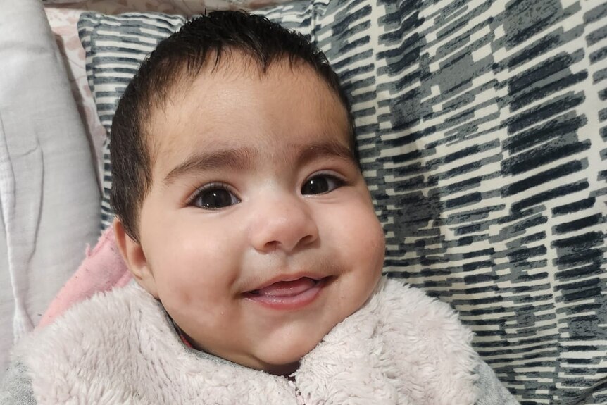 Bhavika has big eyes and a gorgeous smile, looking at the camera from her bassinet.