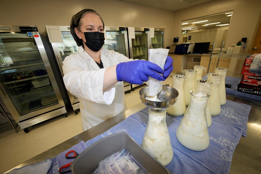 A woman fills a beaker with frozen breast milk from a packet 