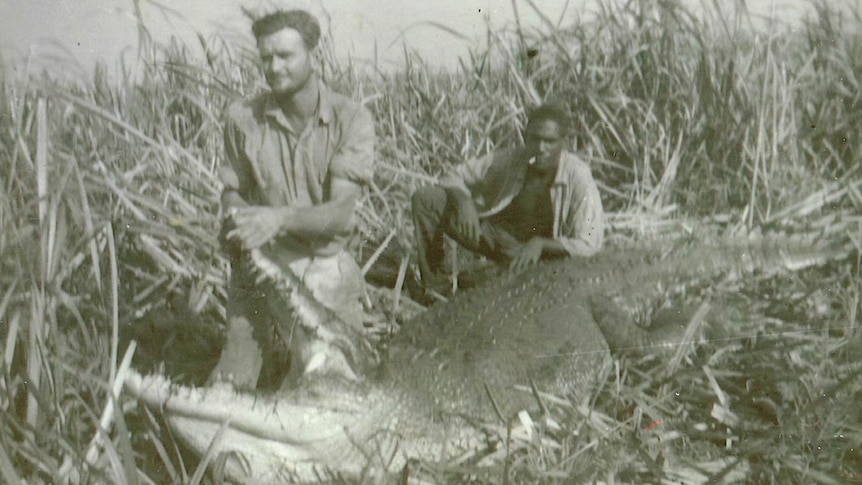 Two men sit with a crocodile.