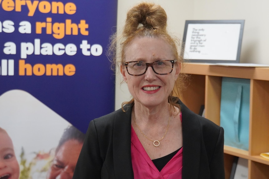 Michelle Mackenzie wears glasses and her auburn hair tied in a high bun while smiling at the camera