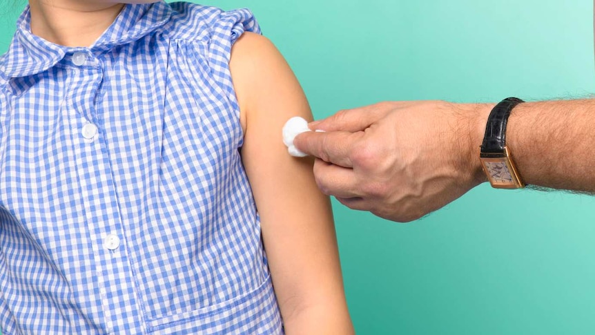 A young girl looks fearfully at a needle