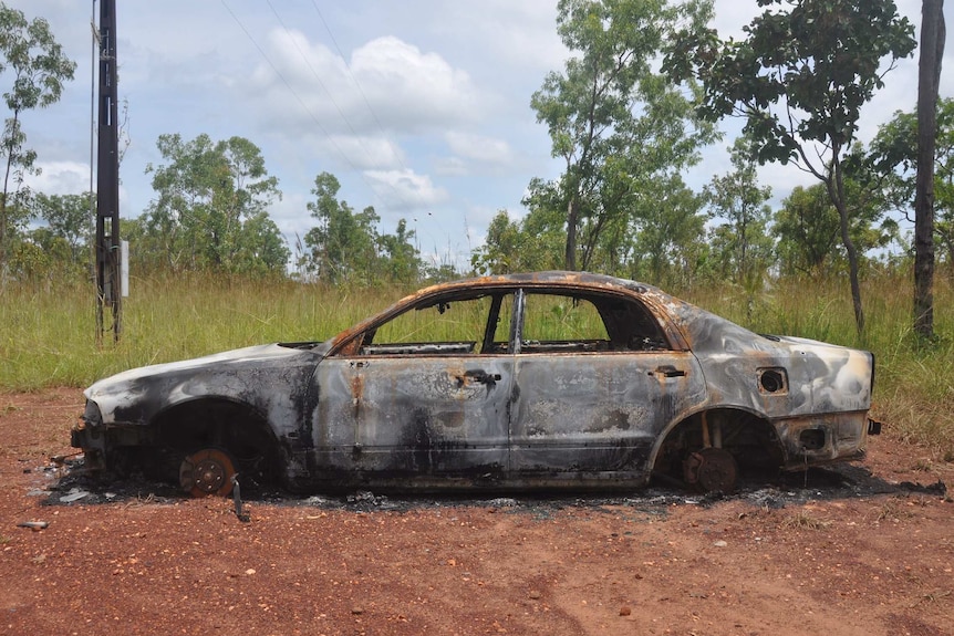 A torched car on a red dirt landscape.