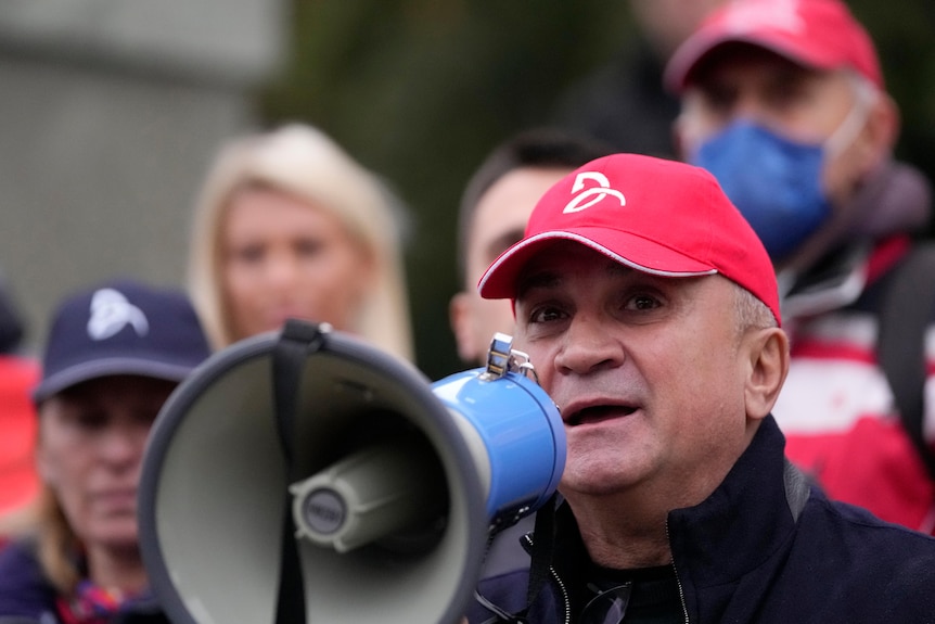 A man in a red baseball cap holds a loudhailer.