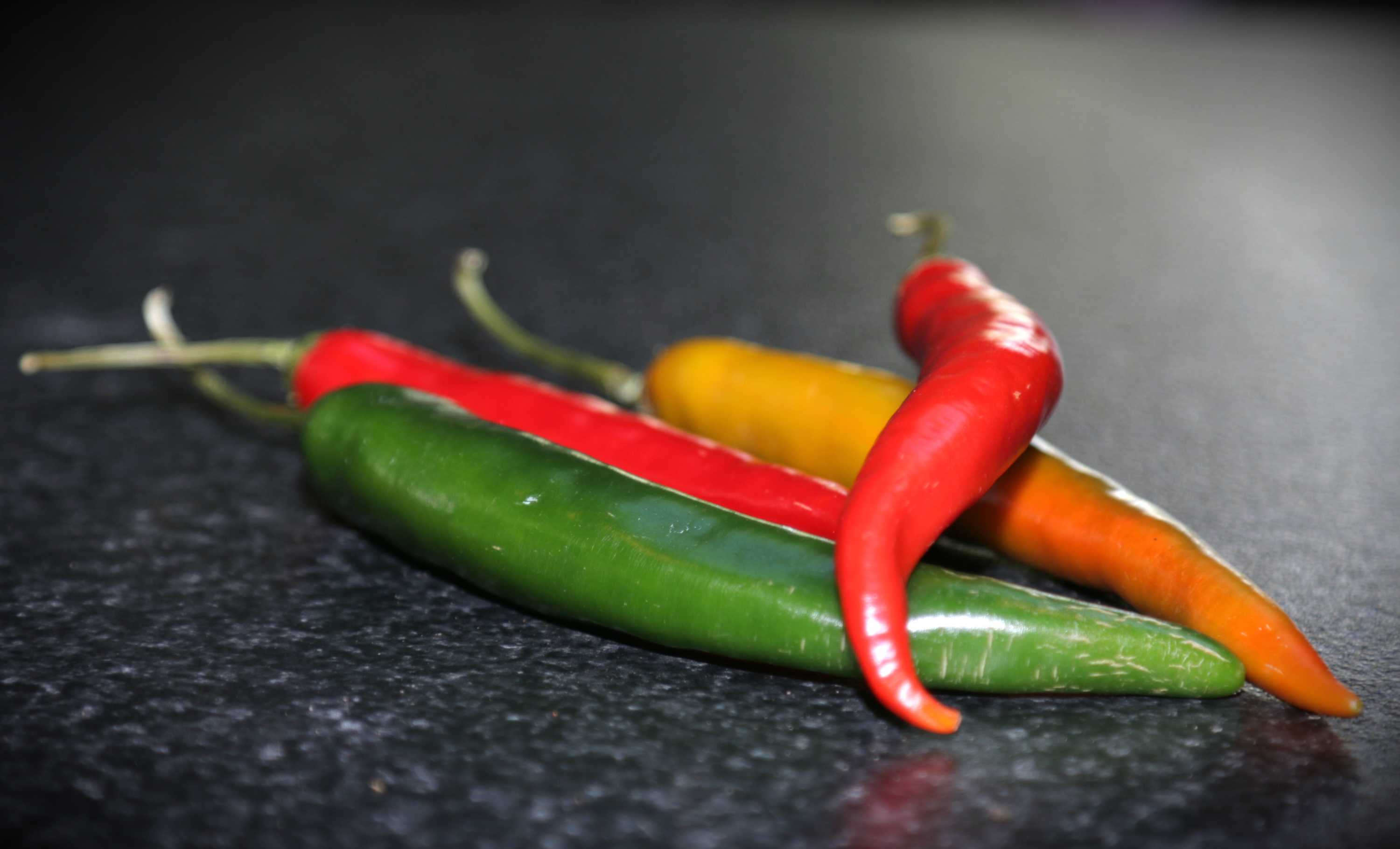 Red, orange and green chillies on a dark bench, representing a DIY vegetable garden that doesn't require a backyard.