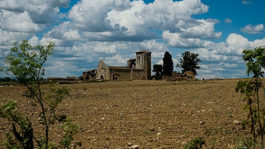 A crumbling medieval church in the distance sits on top of a vast grey field 