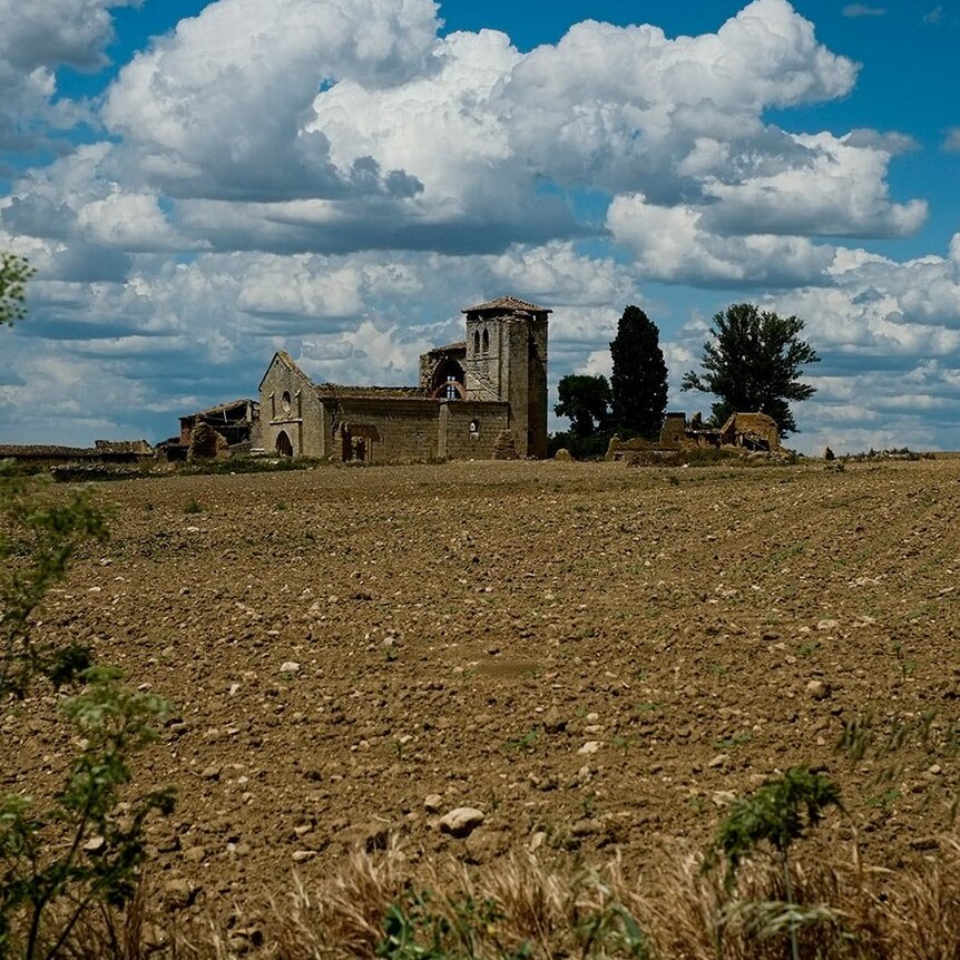 A crumbling medieval church in the distance sits on top of a vast grey field 