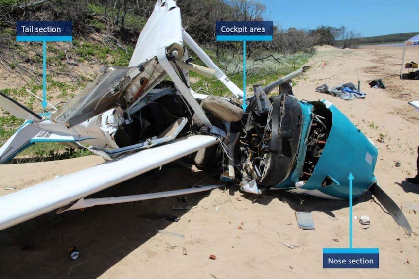 Mangled wreckage of the plane sits on a beach. There are ATSB annotations pointing out sections of the plane.